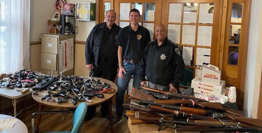 hundreds of guns on tables with three people behind them