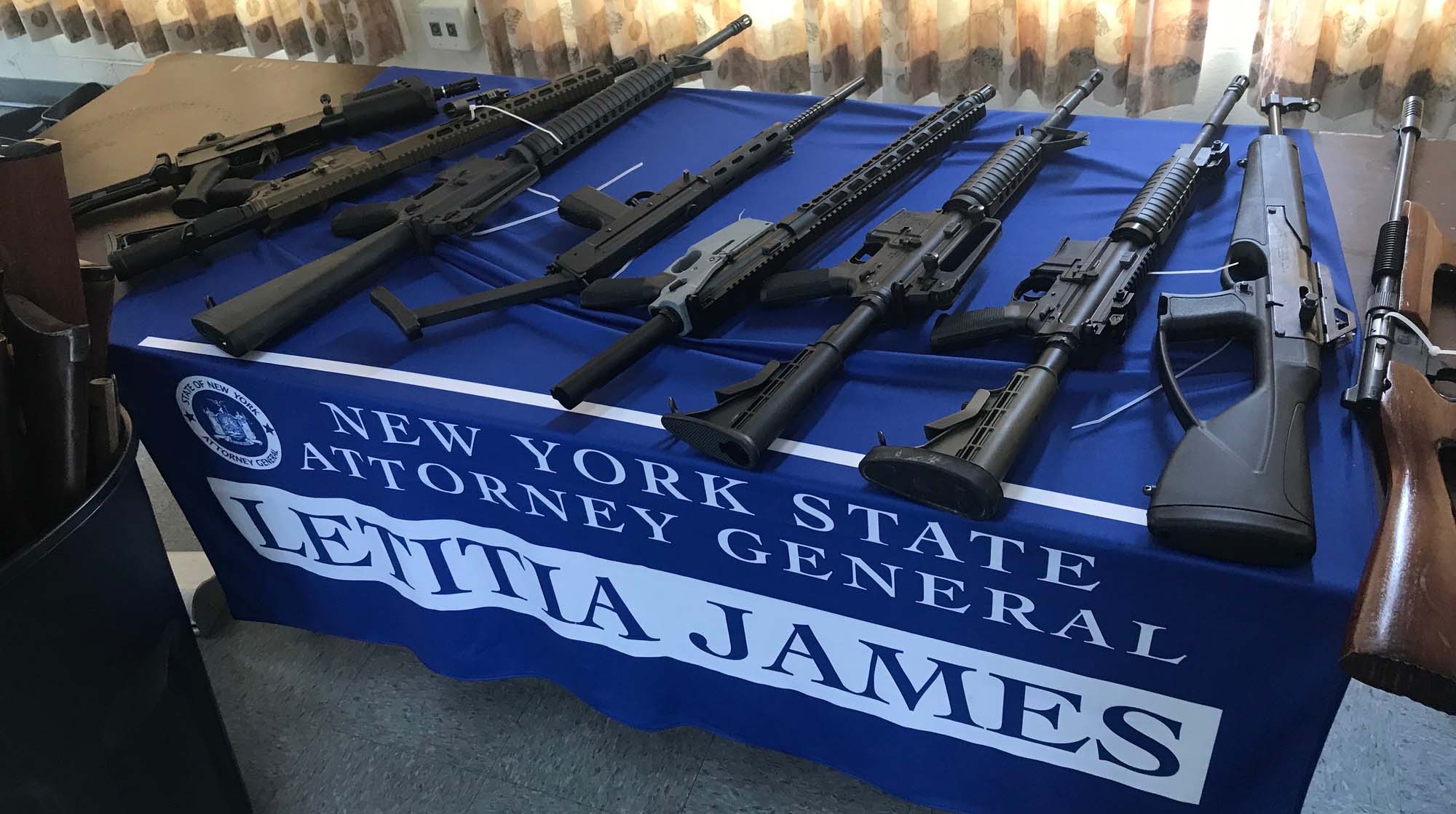 several assault rifles on a table with a blue table cloth
