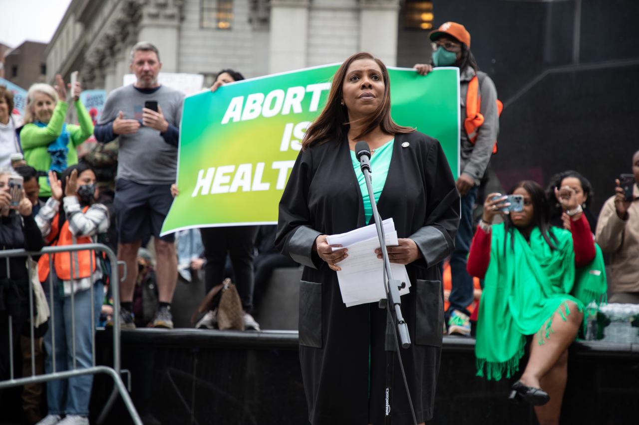 Attorney General James attends a rally and speaks to a crowd. Behind her two protestors hold a sign that reads "Abortion is Healthcare". 