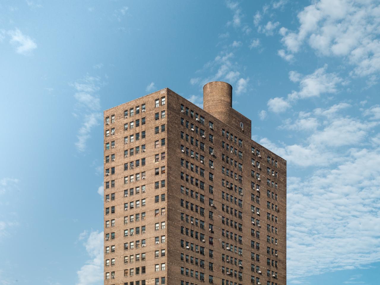 The top half of a simple brick high rise apartment complex against a blue sky