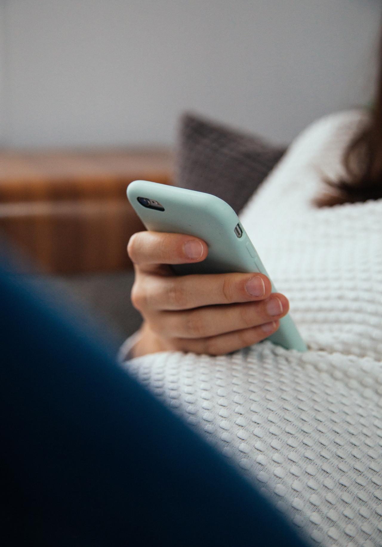 A n image of a person in a white sweater holding a phone with a aqua case using only one hand