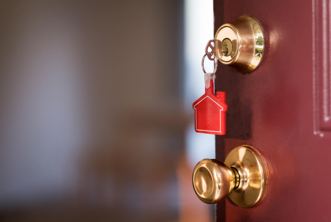 An image of a key inside of a dark red door. They key has a red house decoration on the chain.