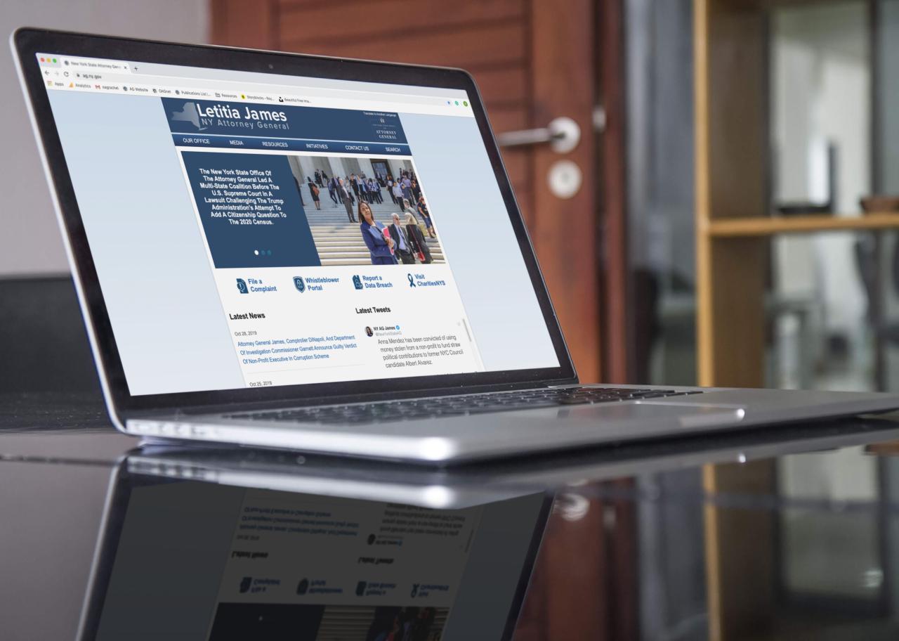 An image of an open laptop on a black table showing the office of the attorney general home page