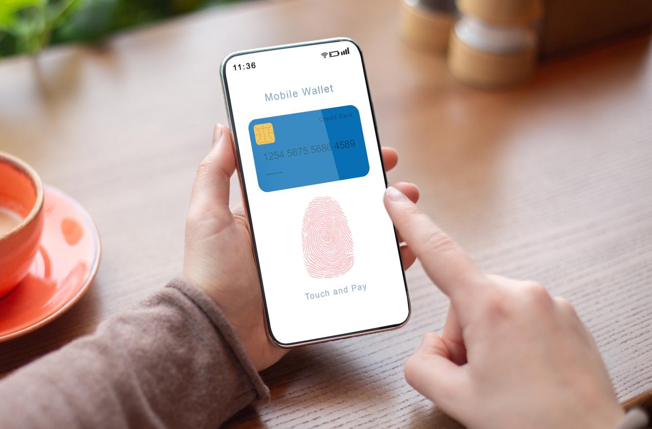 An image of someone holding a smart phone. On the screen of the smart phone there is a digital debit/credit card and a fingerprint.