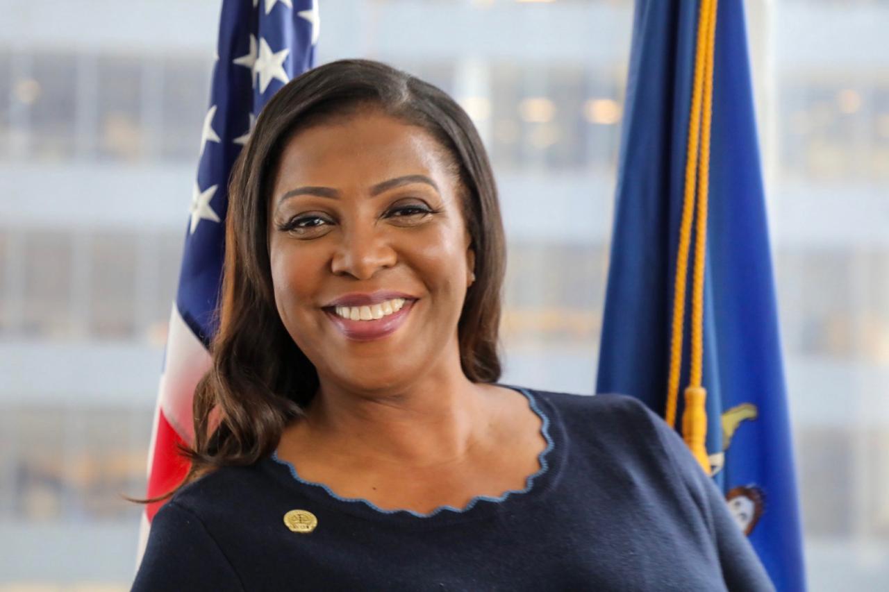 Headshot of Attorney General Letitia James. James stands in front of the American flag and the seal of the State of New York flag. She sits between the two flags and smiles at the camera. 