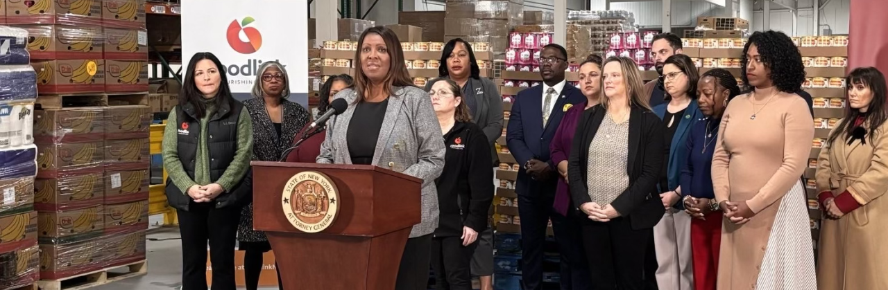 AG James standing a a podium with a group of people and stacked baby forumla behind her