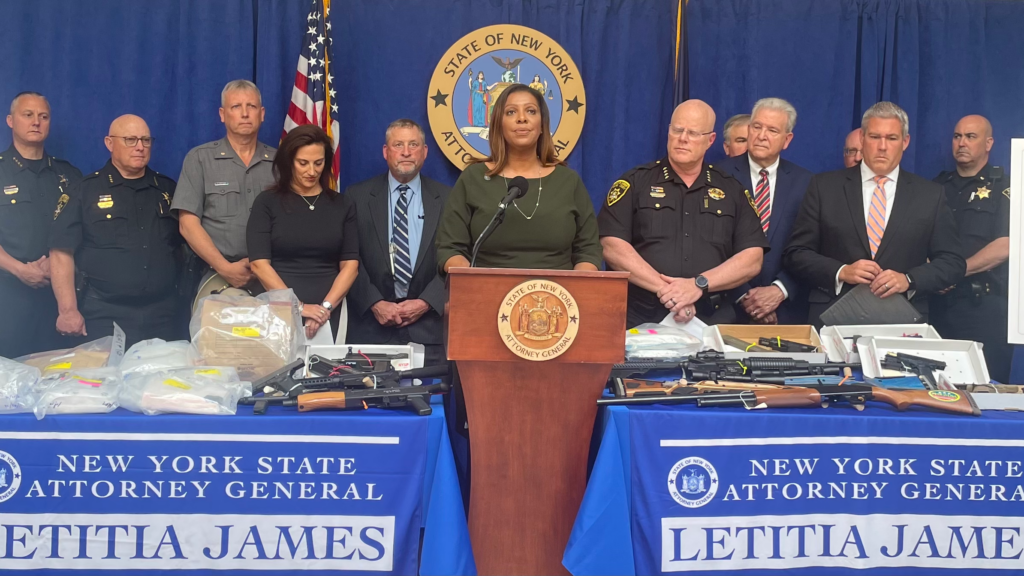 AG James with police and others behind podium displaying some guns they have found