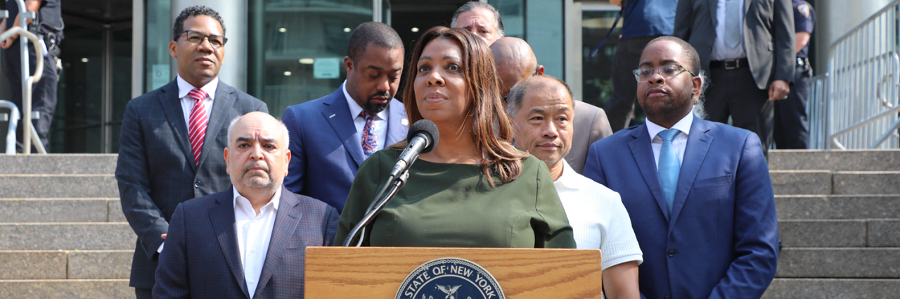 AG James at a podium with a group of people behind her