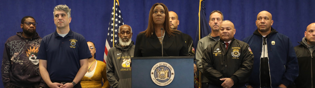 AG James at a podium with a group of people behind her