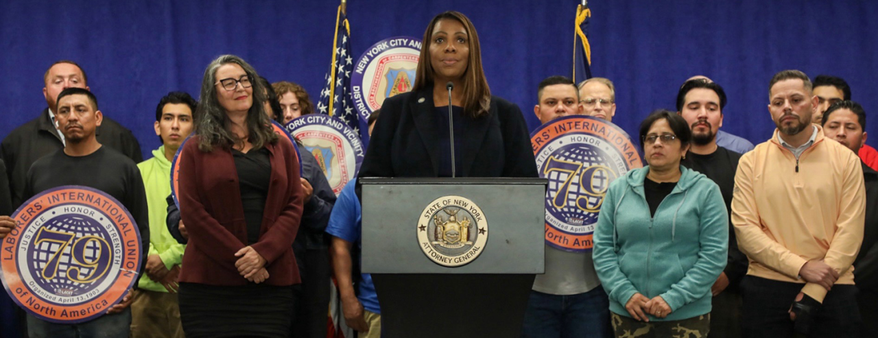 AG James at a podium with a group of people behind her