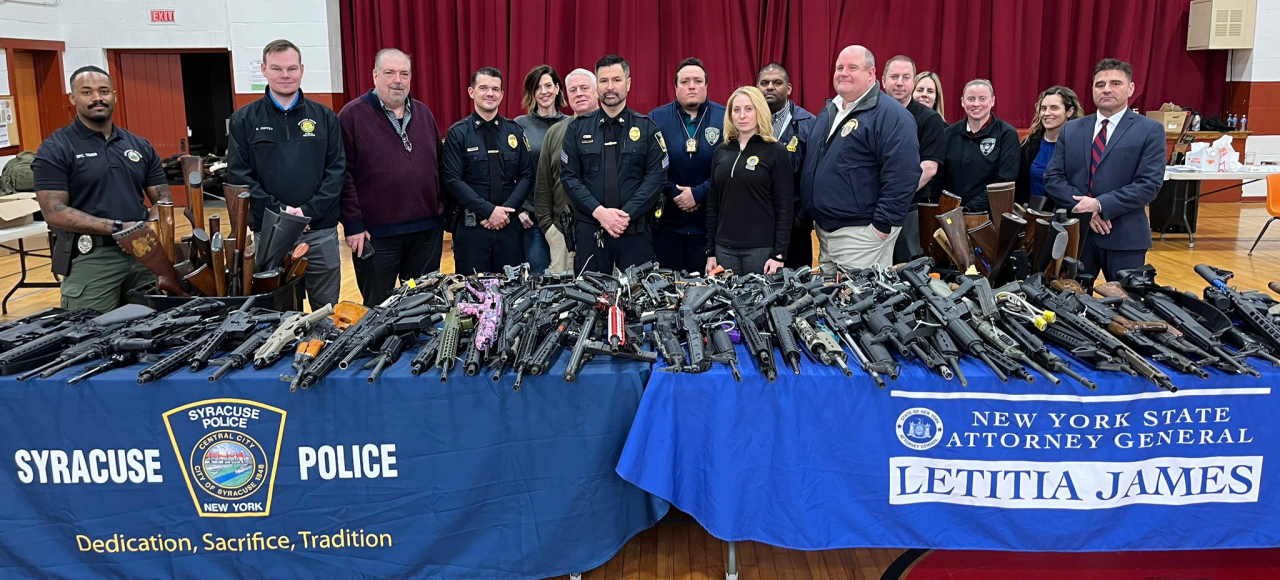 A group of people standing in front of tables filled with guns turned in