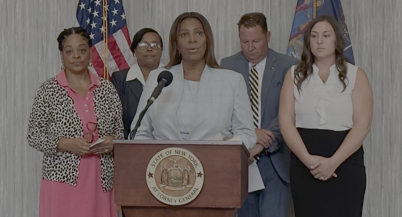 AG James at a podium with a group of people behind her