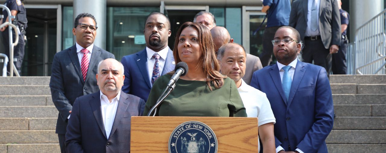 AG James at a podium with a group of people behind her