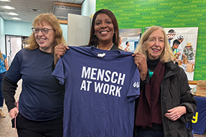 AG James holding up a t-shirt that reads MENSCH AT WORK