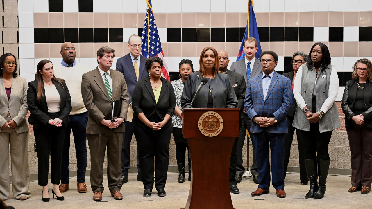 AG James at a podium with a group of people behind her