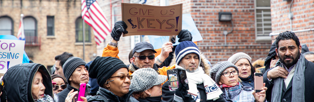 a group of people with in front of brink buildings, one person holding a sign that reads "Give us our keys"