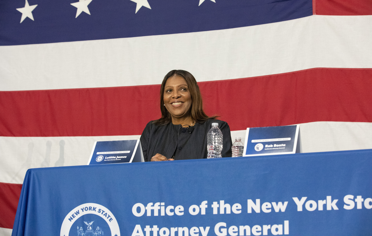 AG James sitting at a table in front of a large American flag